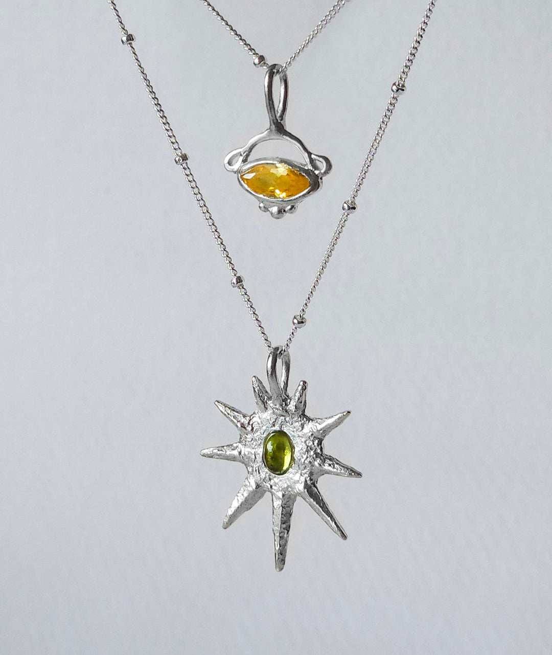 Two silver pendants with gemstones on a light gray background